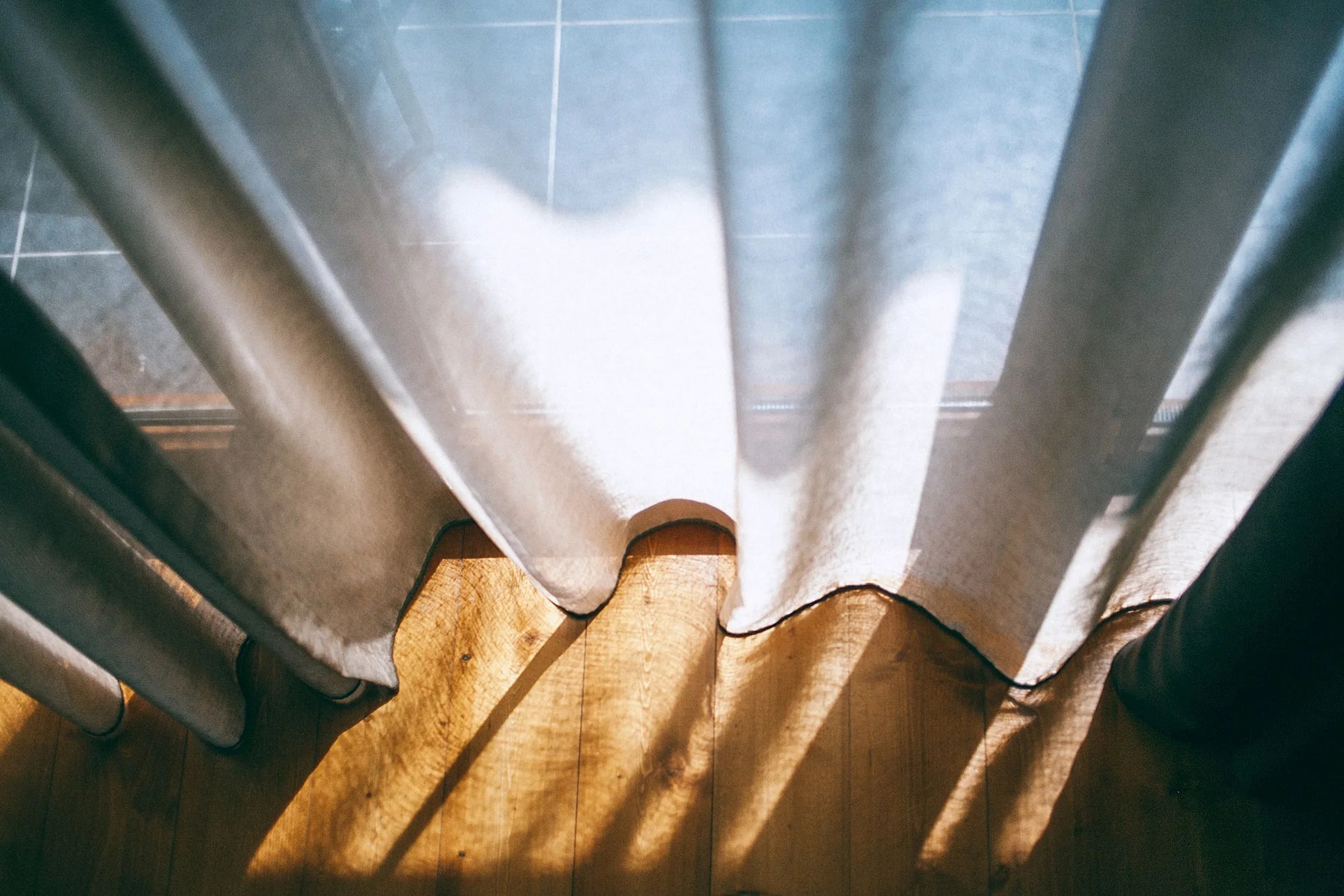 Sunlight crossing translucent white curtains and a wooden floor
